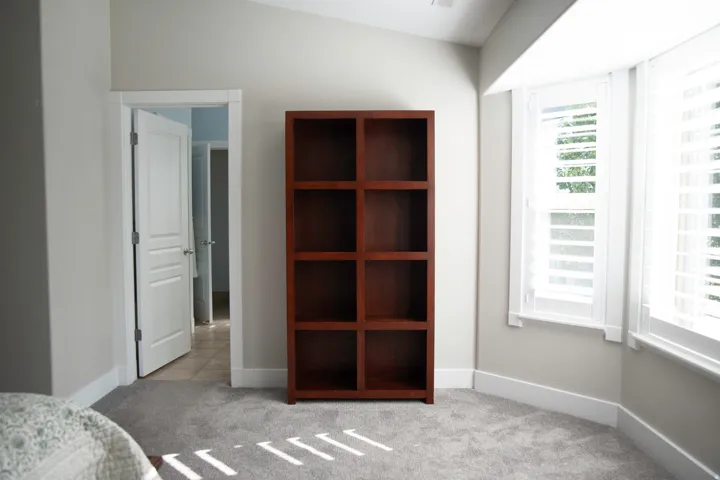 Bay window with plantation shutters and white trim, neutral-toned walls, and grey carpet flooring