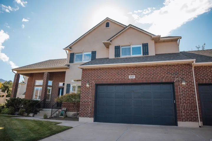 Brick and stucco exterior with a multi-car garage, established front landscaping, and a covered porch entry