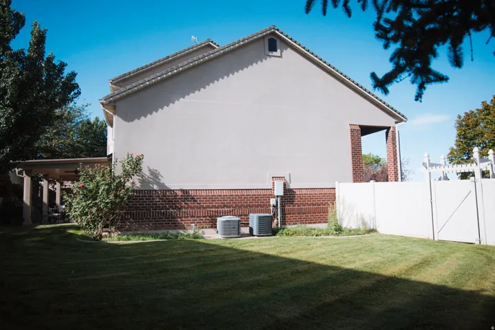 Brick and stucco exterior with a covered patio, gabled roofline, and a white fence