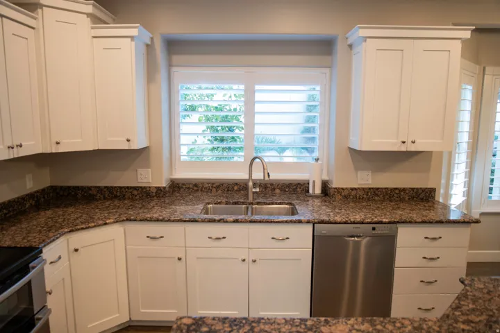 White cabinetry with crown molding, speckled countertops, stainless steel sink with gooseneck faucet, and stainless steel dishwasher