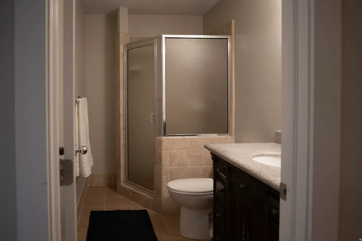 Tiled shower enclosure with frosted glass, tiled flooring, dark wood vanity with integrated sink, and a light-colored countertop