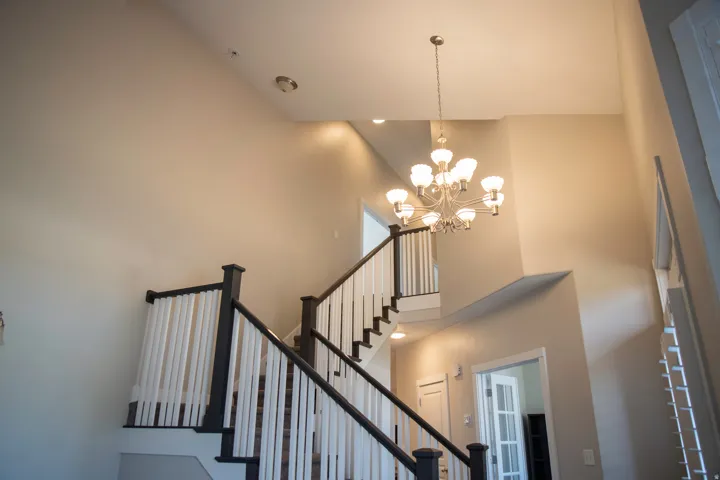 Two-story foyer featuring a multi-tier chandelier, recessed lighting, and a staircase with dark wood newel posts and white balusters