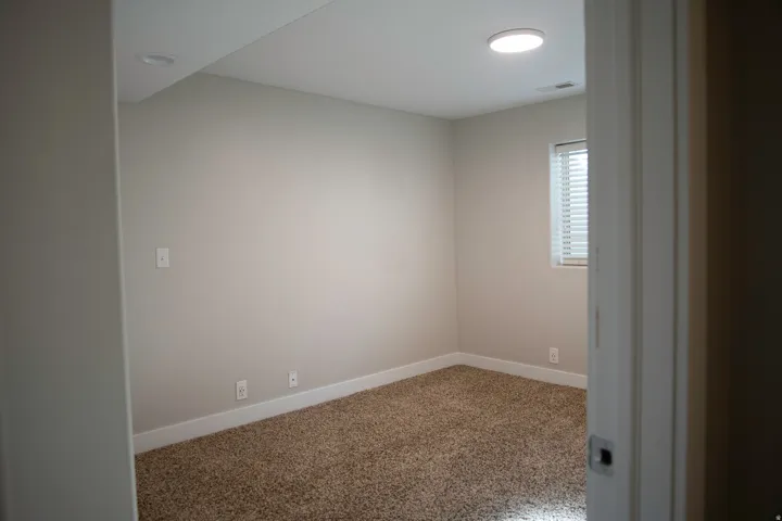 Neutral wall paint, plush carpet flooring, recessed ceiling lighting, and a window with blinds