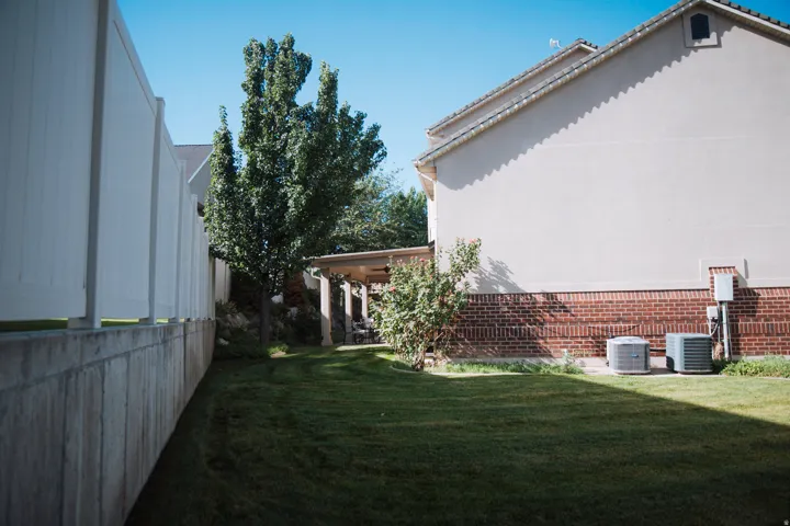 Expansive backyard featuring a manicured lawn, white privacy fencing, and a covered patio area with columns