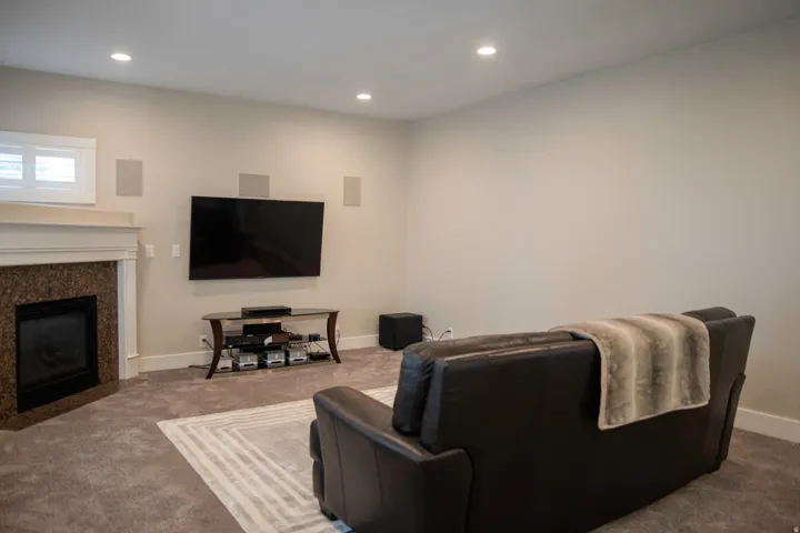 Fireplace with stone surround and classic mantel, recessed lighting, wall-mounted speakers, and a window with white trim