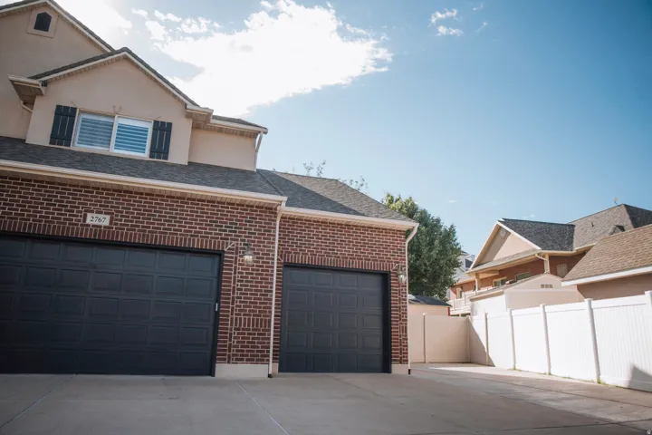 Brick and stucco exterior with two panel garage doors, black window shutters, and a white vinyl privacy fence