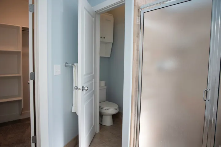 Ensuite half bathroom featuring a glass-enclosed shower, toilet, and wall-mounted storage cabinet