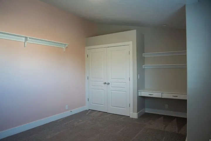 Built-in shelving, integrated desk with drawers, double closet doors, and carpet flooring