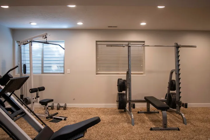 Recessed ceiling lighting illuminates a room with light-colored walls, two windows with horizontal blinds, and textured carpeting