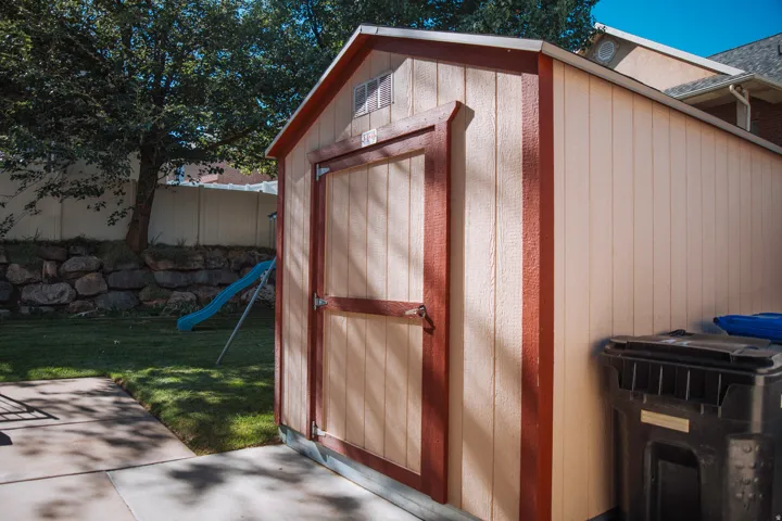 Backyard shed with panel siding and a gabled roof, featuring a single entry door