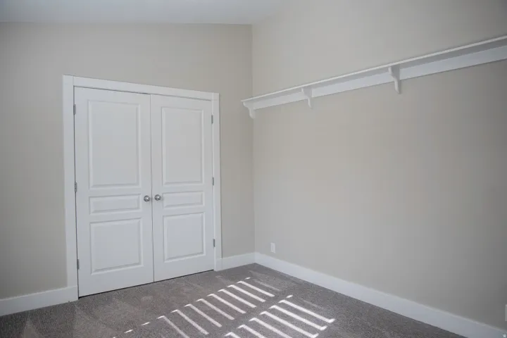 Neutral wall color, wall-to-wall carpeting, white bi-fold closet doors, and integrated closet shelving