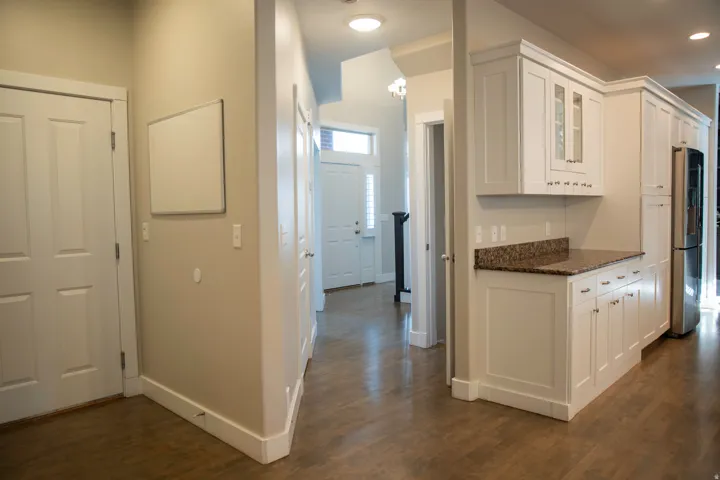 White shaker cabinetry with granite countertops, stainless steel appliances, wood-finish flooring, and crown molding