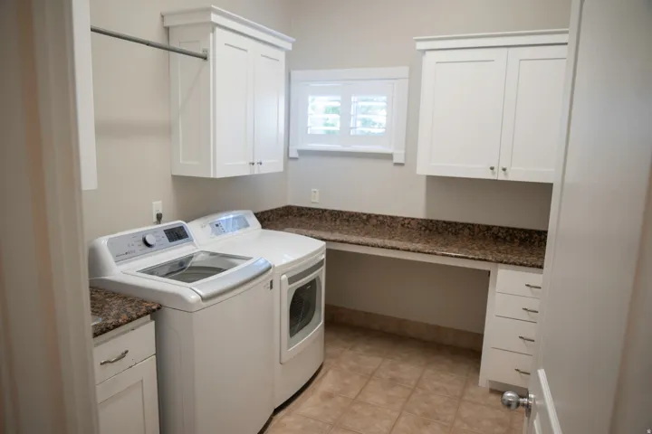 White shaker cabinetry with crown molding, granite-finish countertops, ceramic tile flooring, and integrated laundry appliances