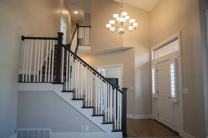 Double entry door with transom window, vaulted ceiling, wood-finish flooring, two-tone staircase with carpeted treads, and an overhead chandelier