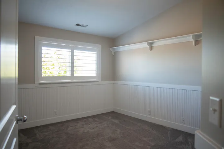 Room featuring wainscoting, plantation shutters, wall-mounted shelving, and carpet flooring