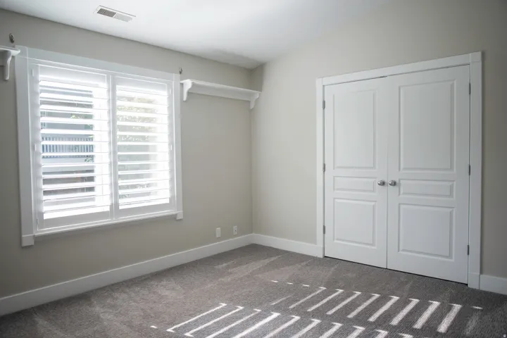Carpeted flooring, white interior doors, window with louvered shutters, and wall-mounted shelving
