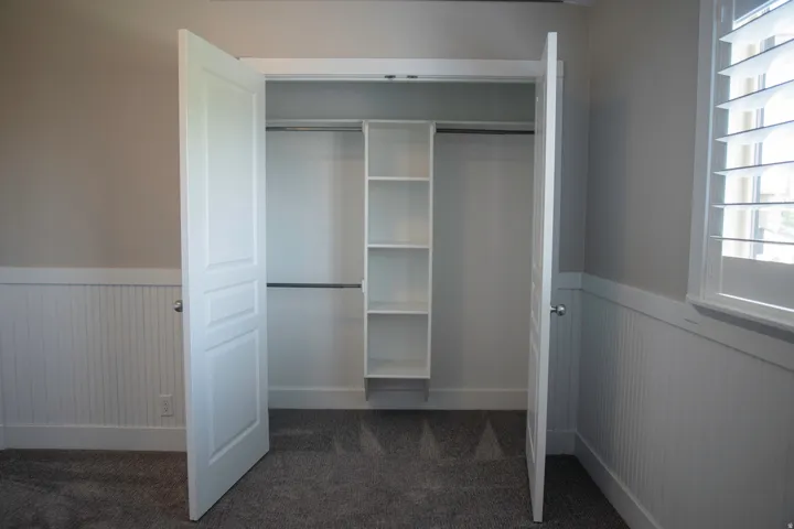Double-door closet with built-in shelving and hanging rods, complemented by wainscoting and carpet flooring