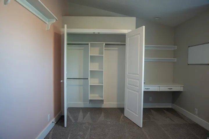 Built-in desk with dual drawers, custom shelving, integrated closet organization, and neutral carpeting
