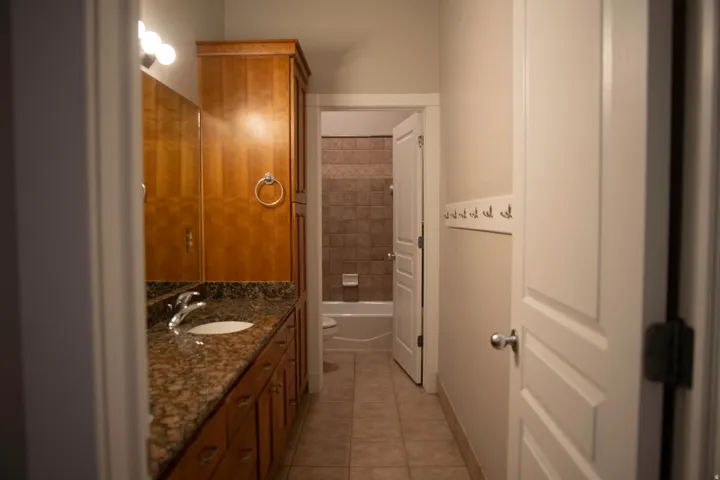 Bathroom vanity with an integrated sink, stone countertop, wood cabinetry, and a mirrored wall