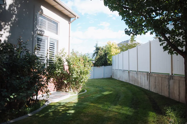 Expansive lawn area with mature perimeter landscaping, private vinyl fencing, and a concrete retaining wall