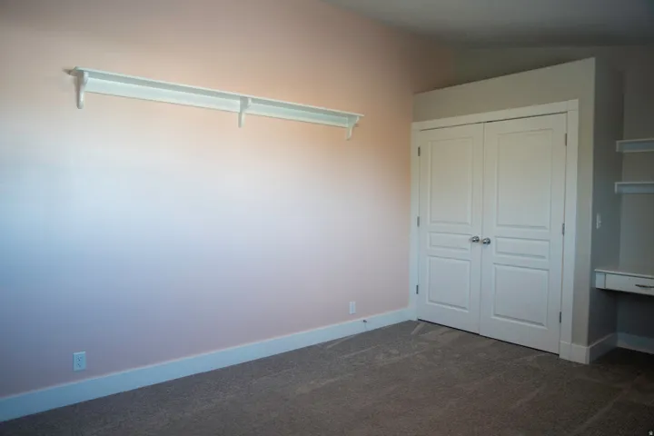 Built-in desk with shelving, painted walls, carpet flooring, and white bi-fold closet doors