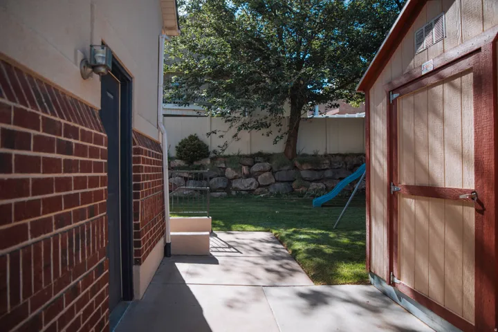 Brick exterior with a side entry door, concrete pathway, and a detached storage shed