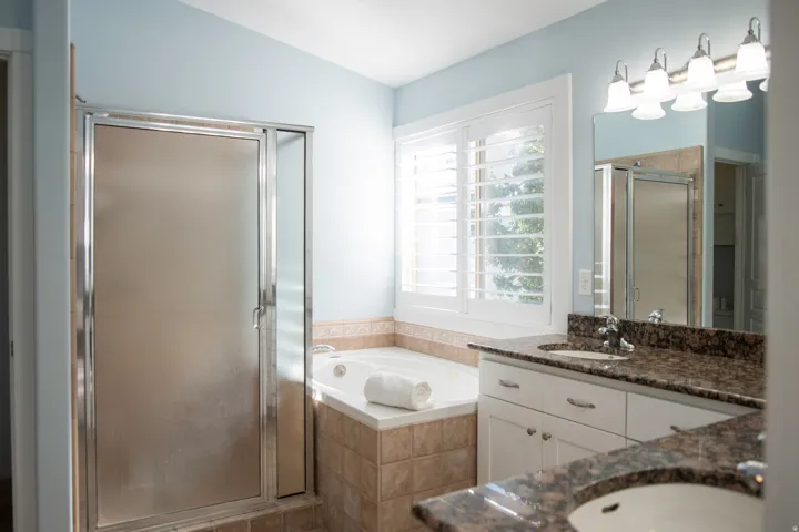 Ensuite bathroom with dual vanity with integrated sinks, framed mirror, and mounted light fixture