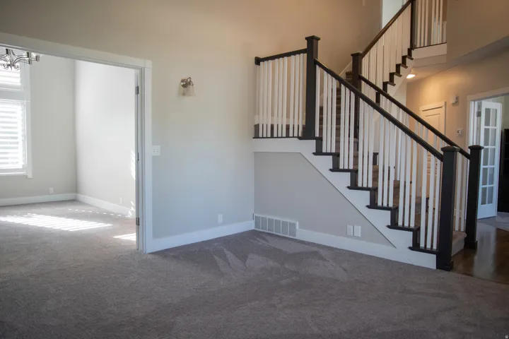 Carpeted flooring, multi-story staircase with dark wood-finish handrails, white balusters, and a wall-mounted light fixture