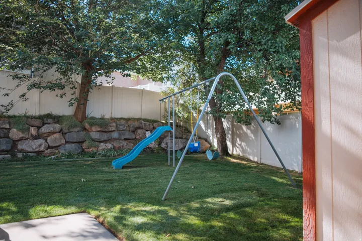 Expansive backyard featuring a manicured lawn, mature trees, and a stone retaining wall