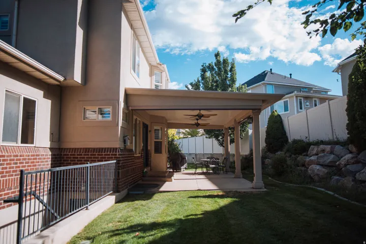Expansive covered patio with ceiling fans, concrete flooring, and decorative columns