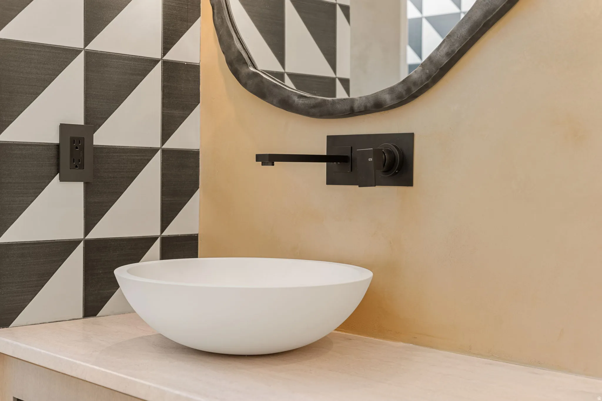 Vessel sink with a wall-mounted matte black faucet, set against a geometric tiled backsplash and a light-toned countertop