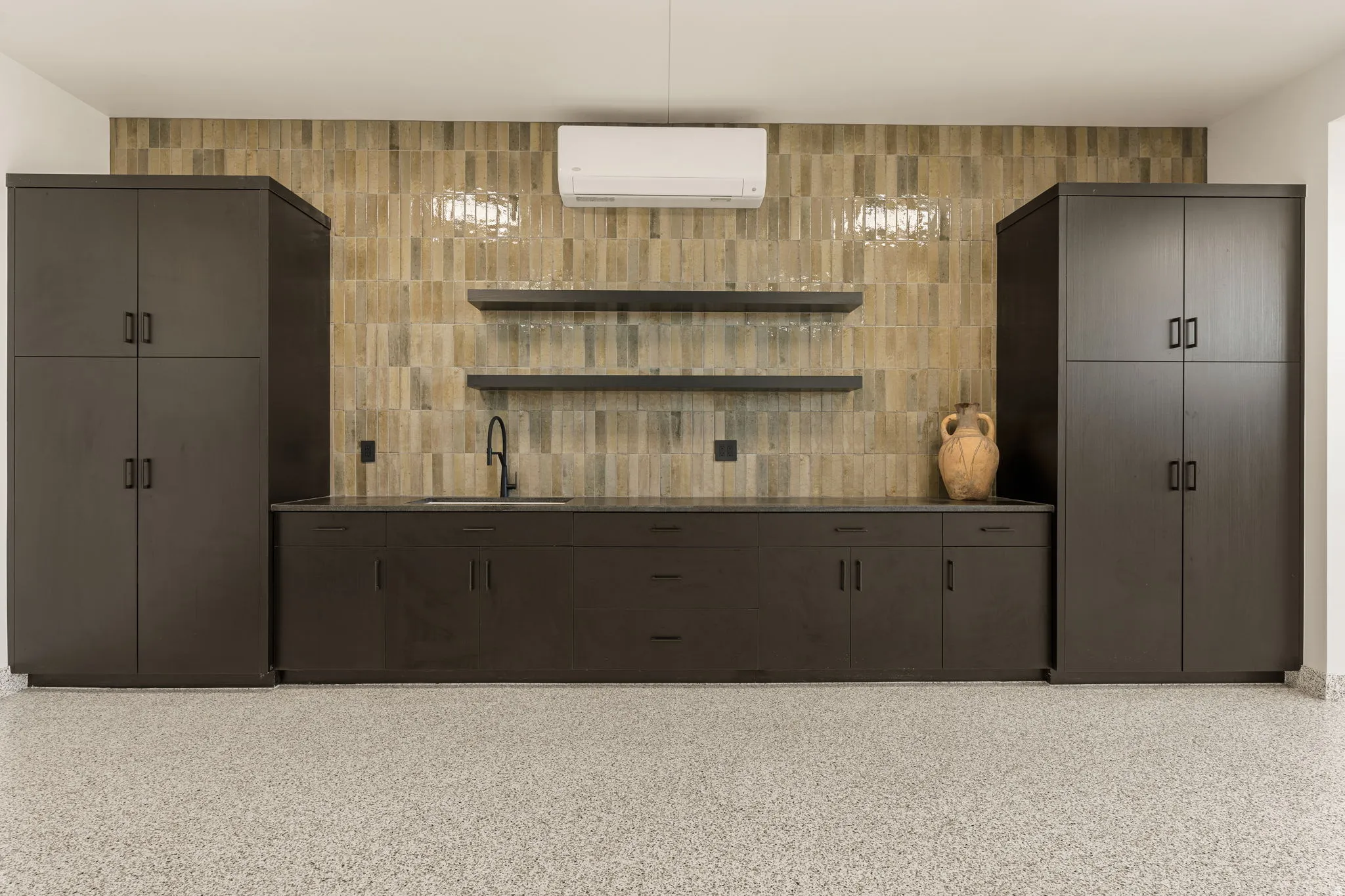 Built-in dark cabinetry with integrated sink, two floating shelves, and a textured tile backsplash