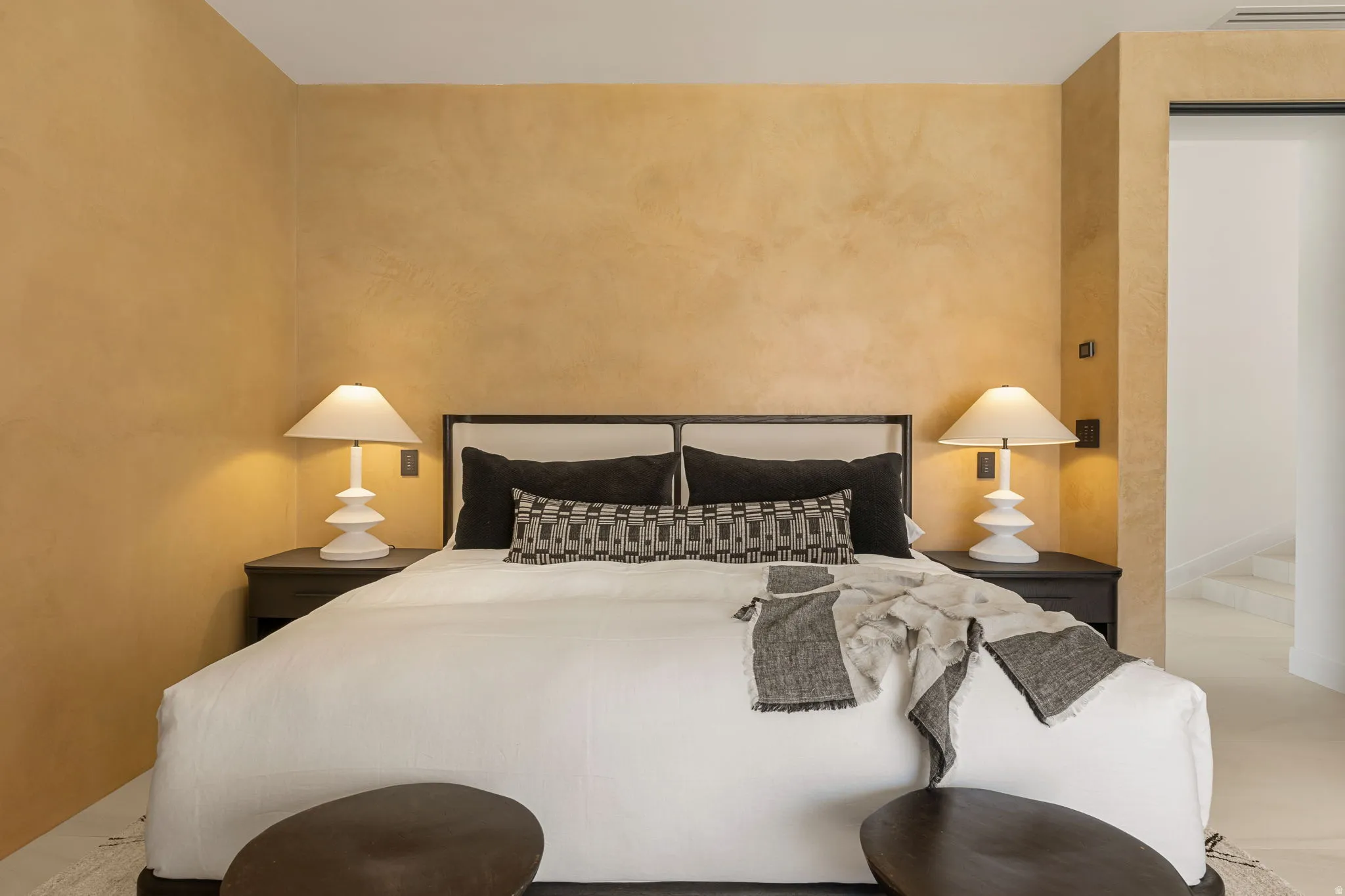 Textured wall finish, built-in recessed lighting, dark wood-finish nightstands, upholstered bed frame, and light flooring