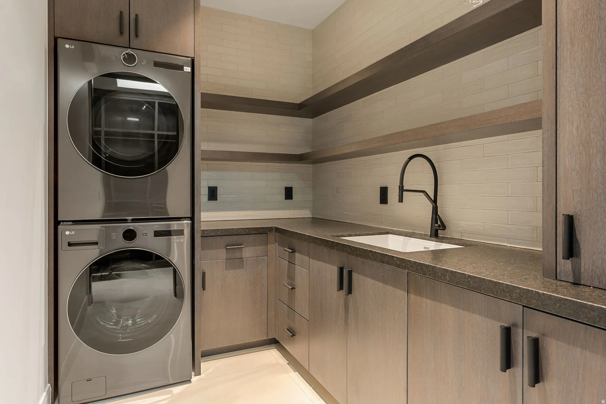 Built-in cabinetry with dark hardware, undermount sink with a matte black faucet, and stacked washer and dryer