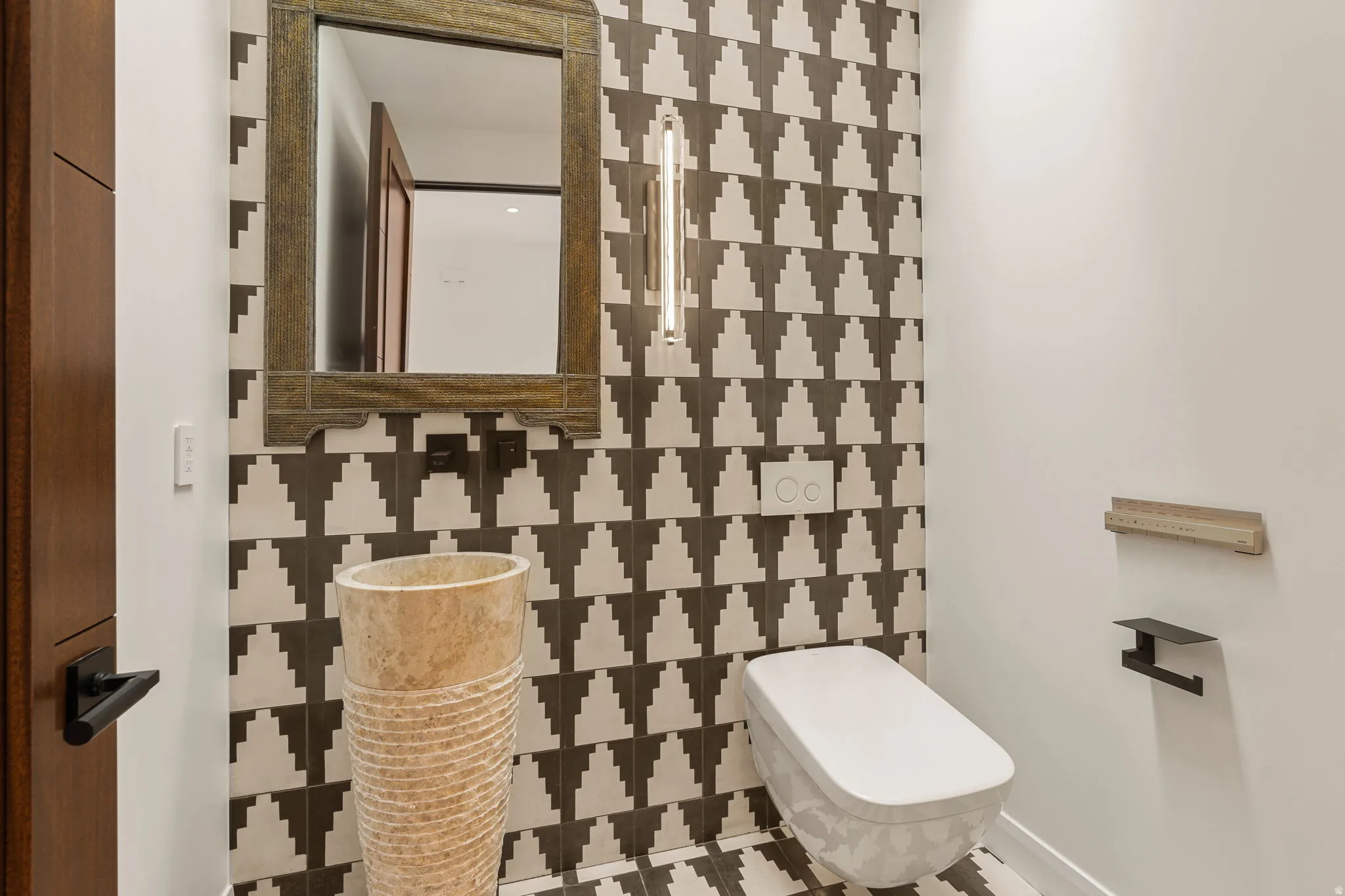 Powder room featuring a pedestal basin, wall-mounted toilet, decorative tile accent wall, and a framed mirror