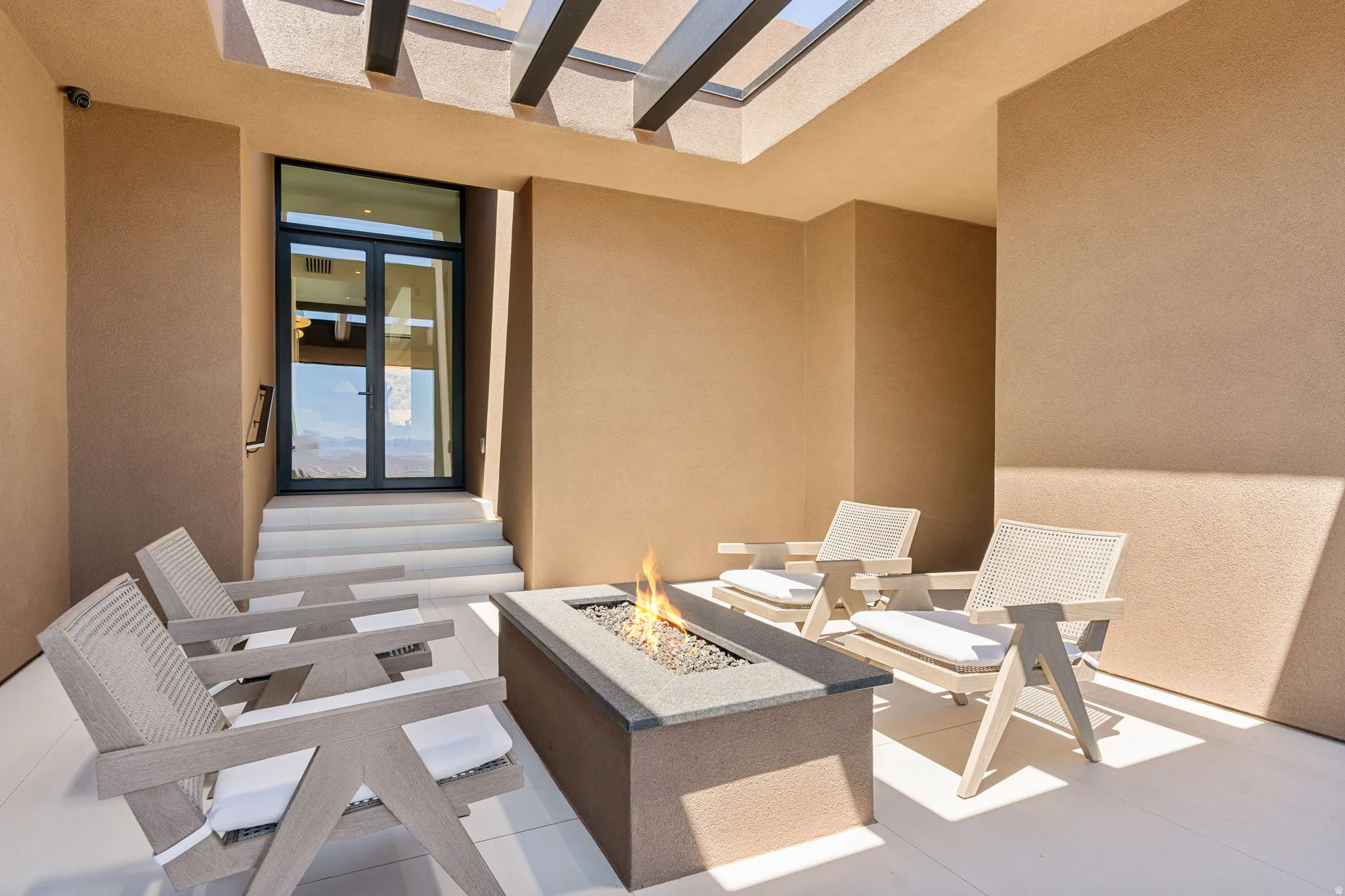 Private outdoor patio featuring a linear fire pit, overhead pergola, and light-toned tile flooring
