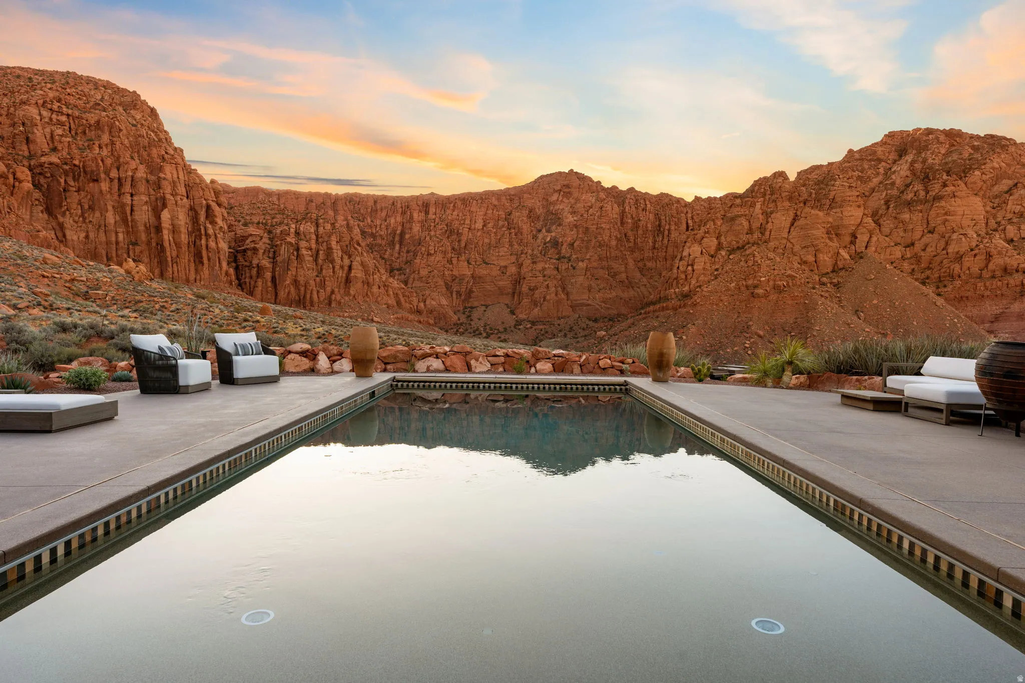 Expansive outdoor living area featuring a rectangular swimming pool, concrete decking, and natural rock landscaping