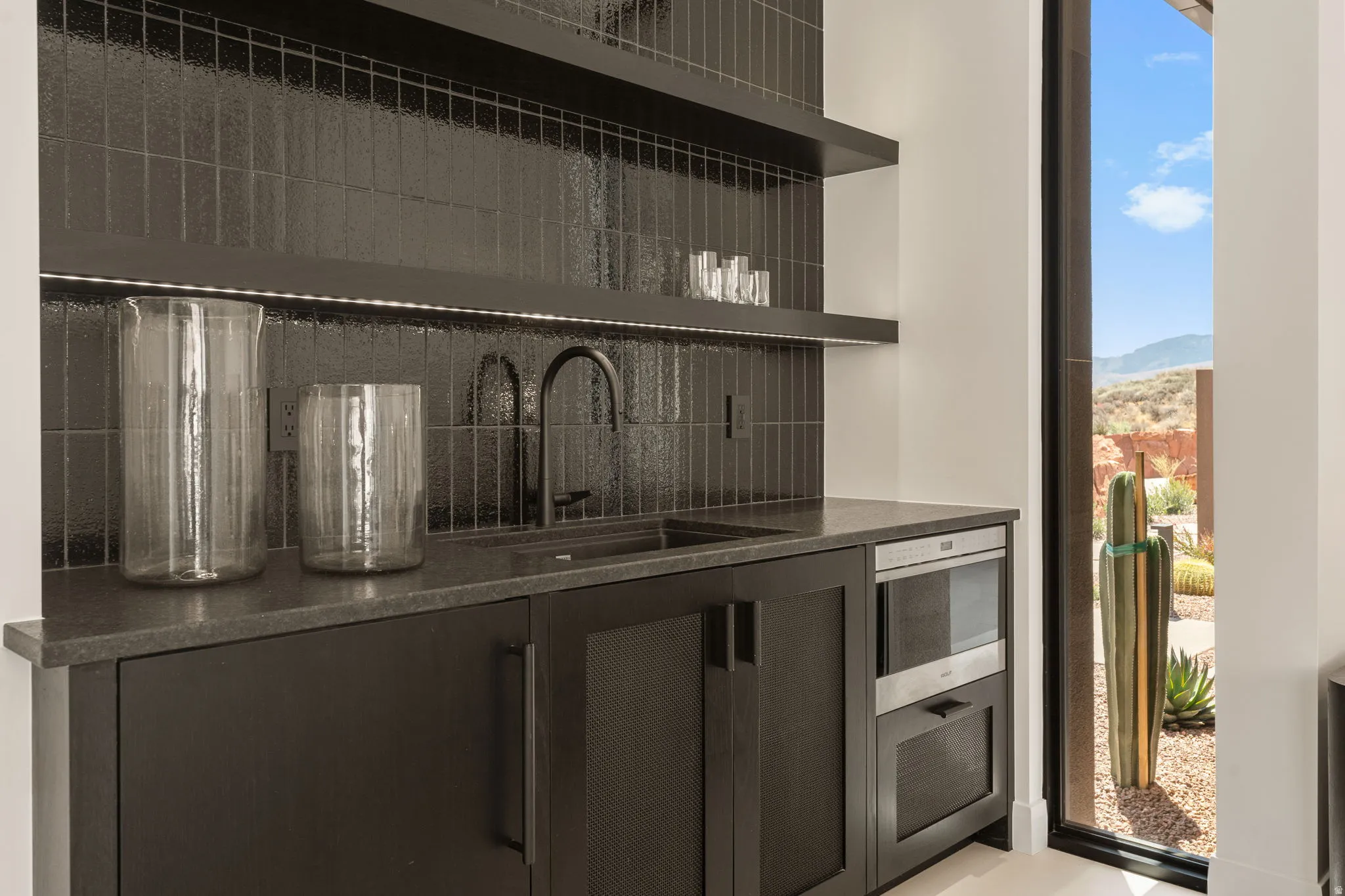 Integrated wet bar featuring dark cabinetry, dark countertop, black tile backsplash, and built-in microwave