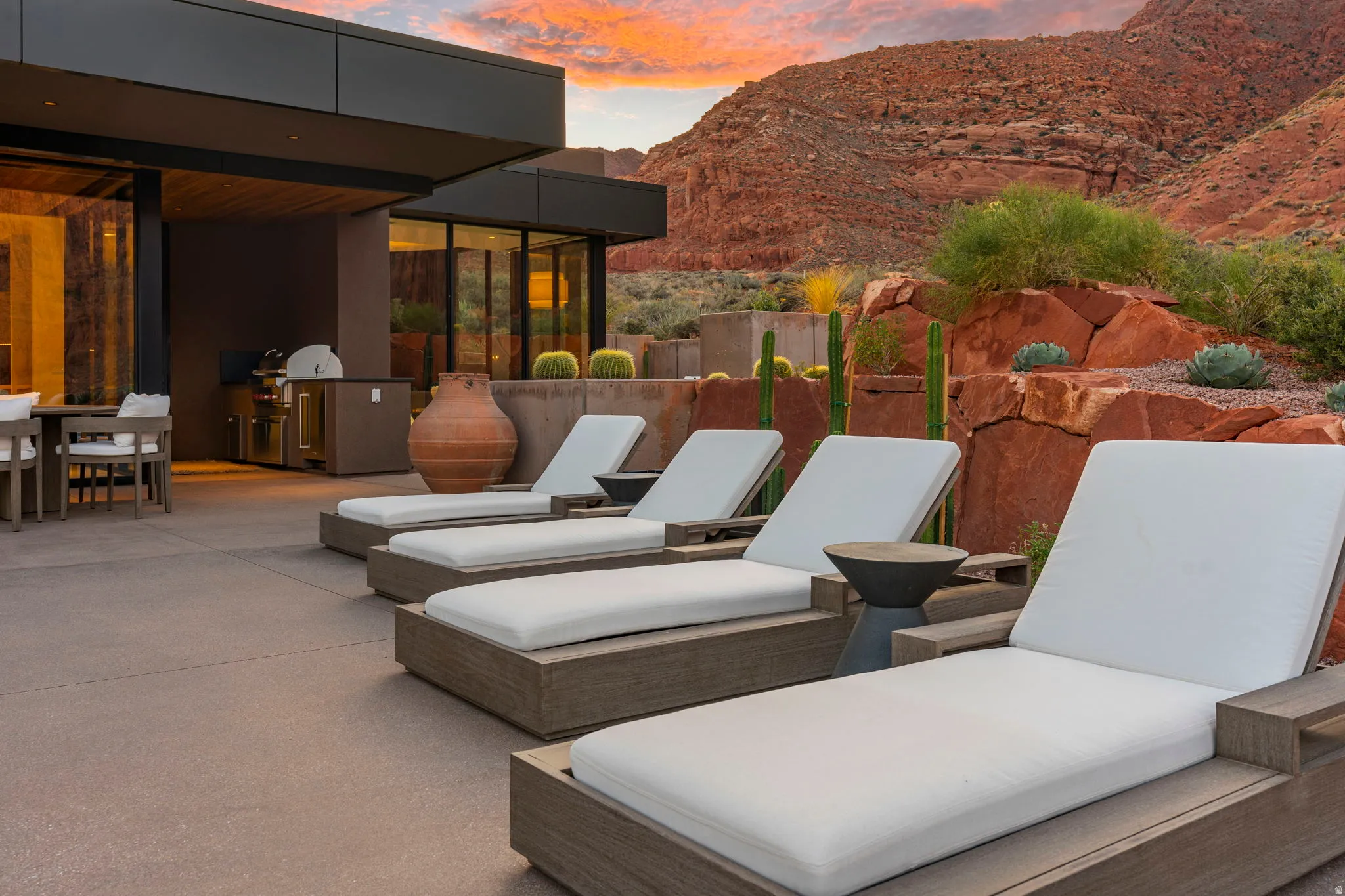 Expansive outdoor patio with a built-in outdoor kitchen, modern architectural design, and integrated desert landscaping featuring natural rock formations and cactuses