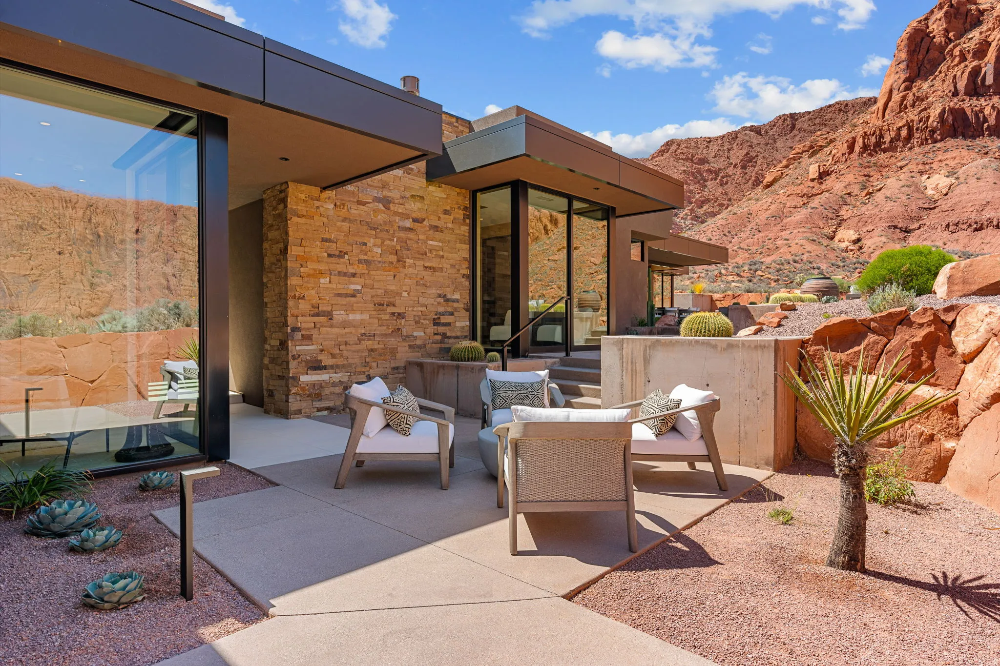 Exterior featuring natural stone cladding, extensive glazing, a concrete patio, and a desert landscape with natural rock formations