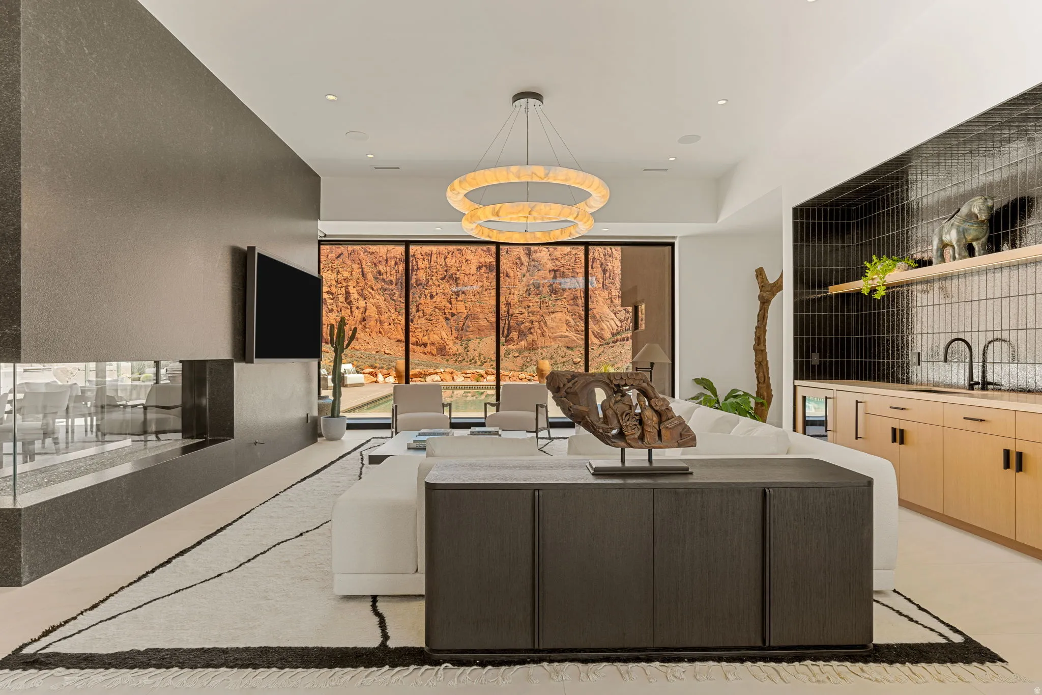 Full-height glass paneling, a linear gas fireplace, a built-in wet bar with wood-finish cabinetry, and a contemporary chandelier