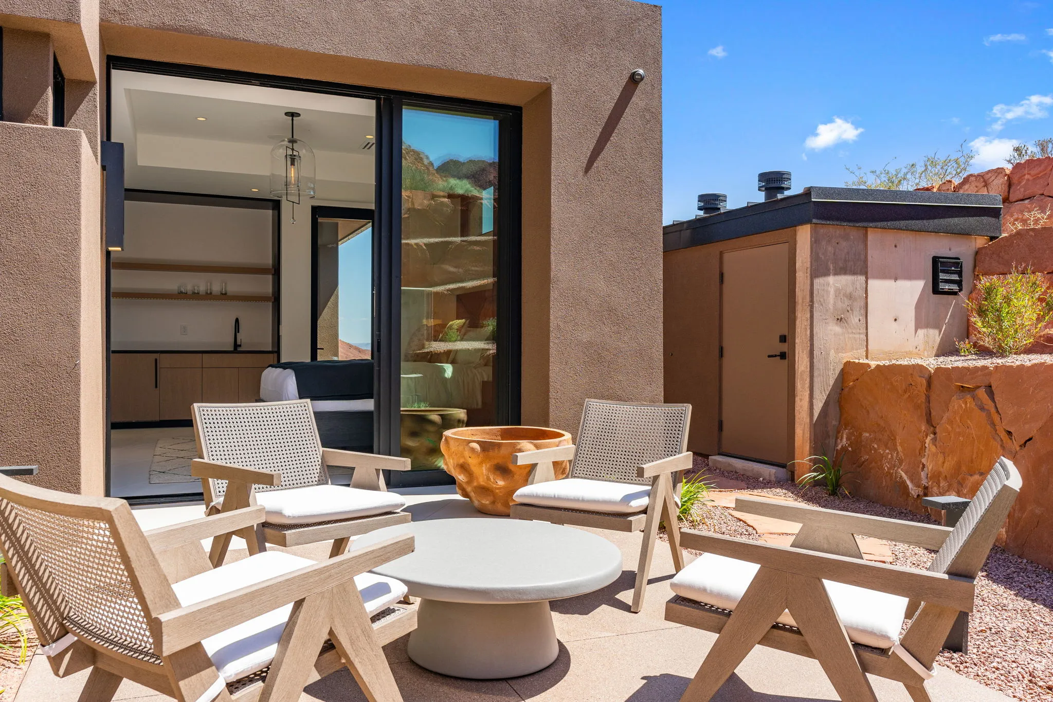 Patio with concrete slab, gravel landscaping, exterior lighting, and sliding glass doors revealing an interior with a built-in wet bar and open shelving