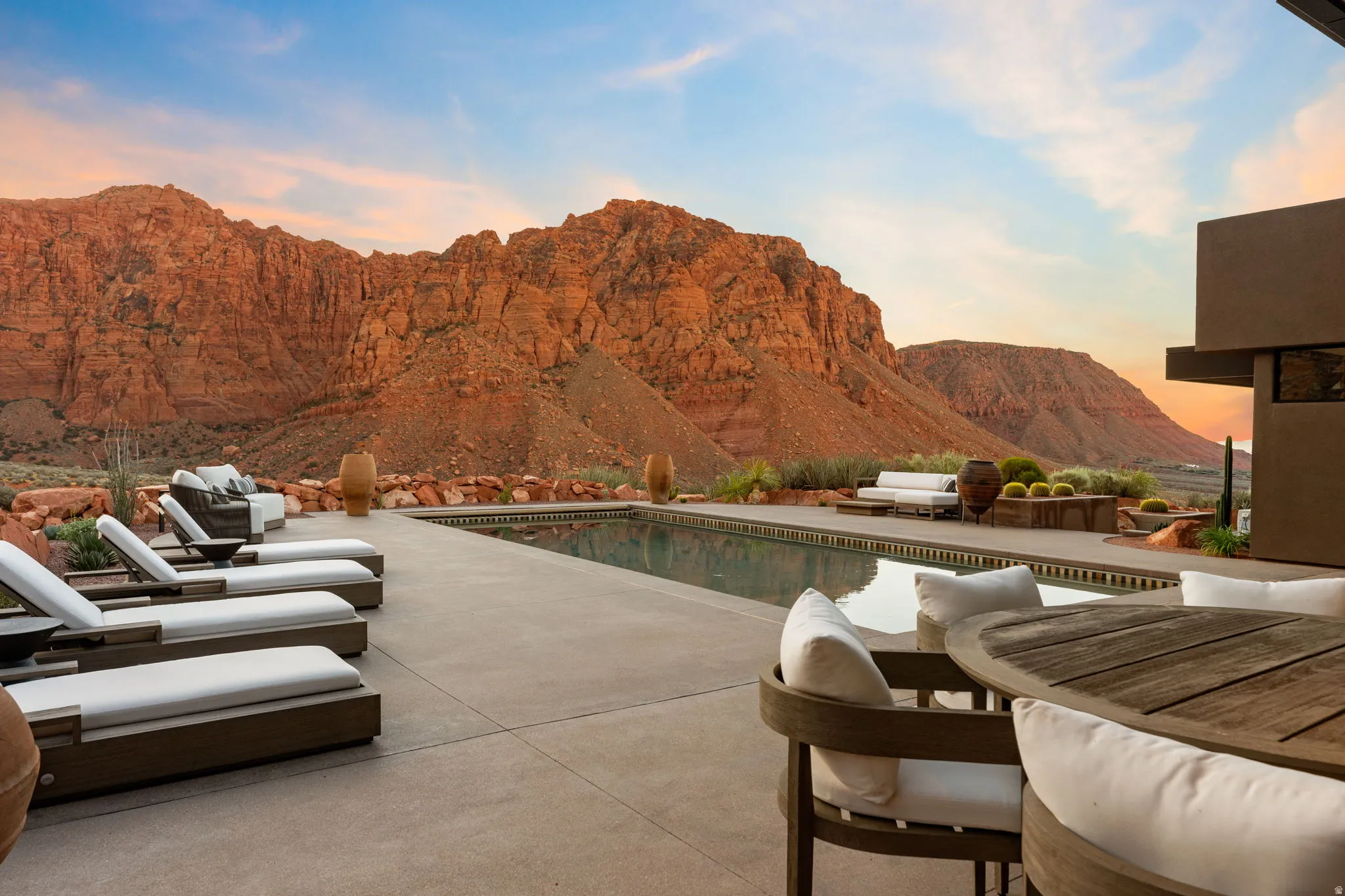 Expansive concrete patio with an integrated swimming pool and desert landscaping, set against a dramatic rock formation backdrop