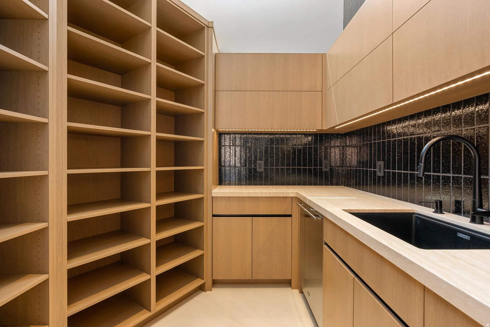 Custom built-in shelving, wood-finish cabinetry, solid surface countertops, a black tile backsplash, and an integrated sink with a matte black faucet