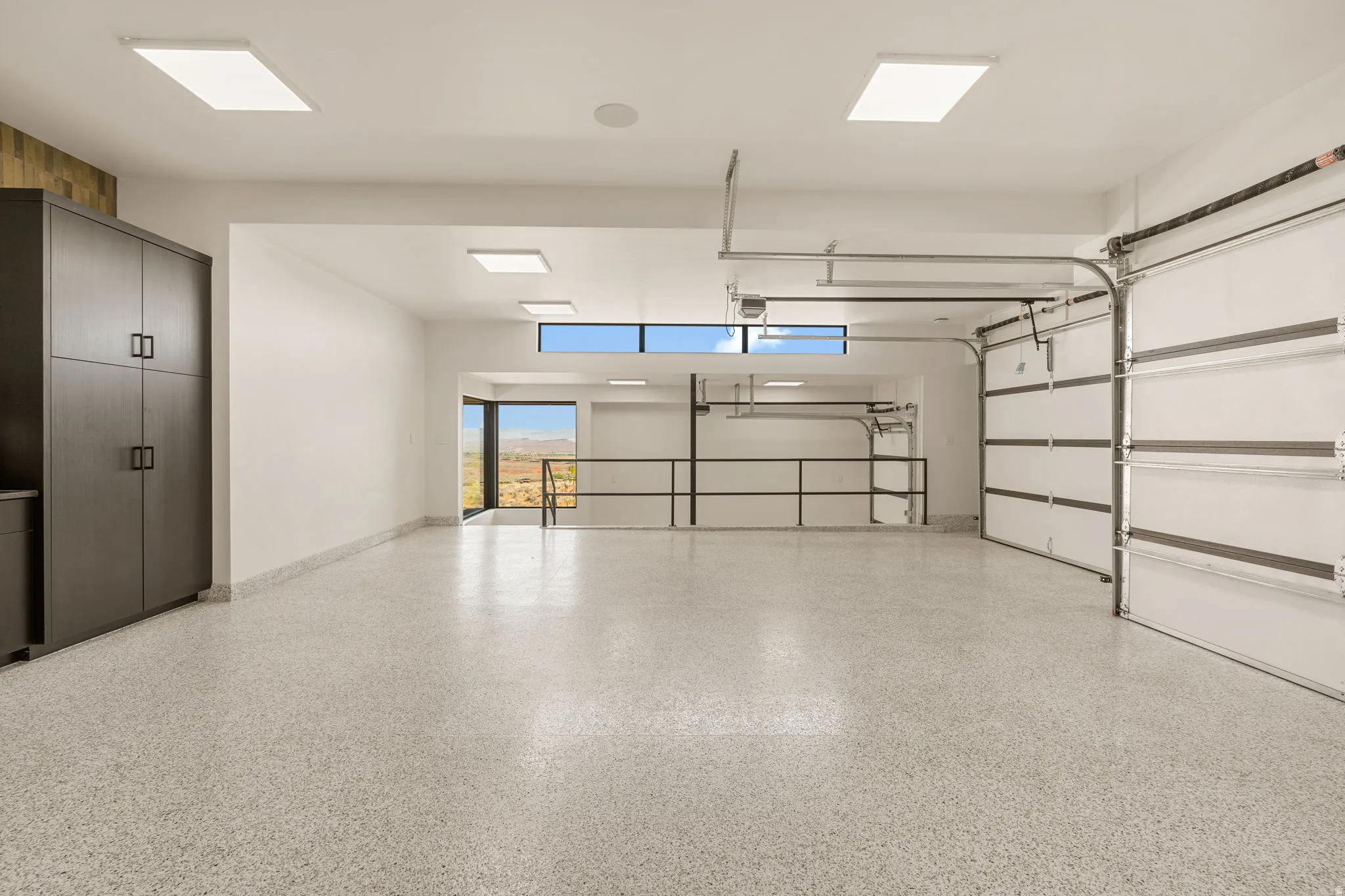 Expansive garage space with a speckled epoxy floor, overhead panel lighting, built-in storage cabinetry, and a large overhead garage door