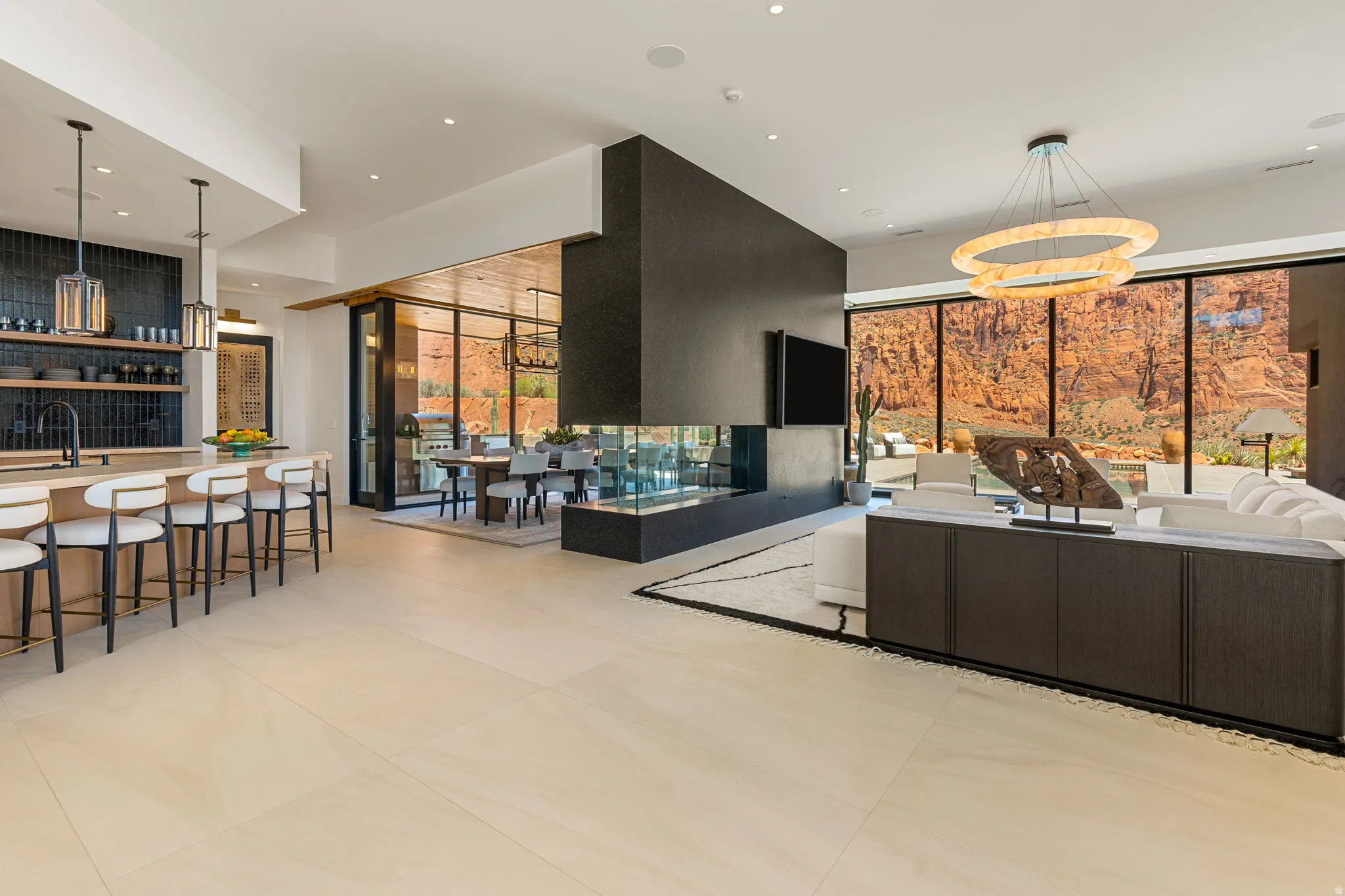 Open-concept living space with light-toned tile flooring, a central multi-sided fireplace, and expansive floor-to-ceiling windows