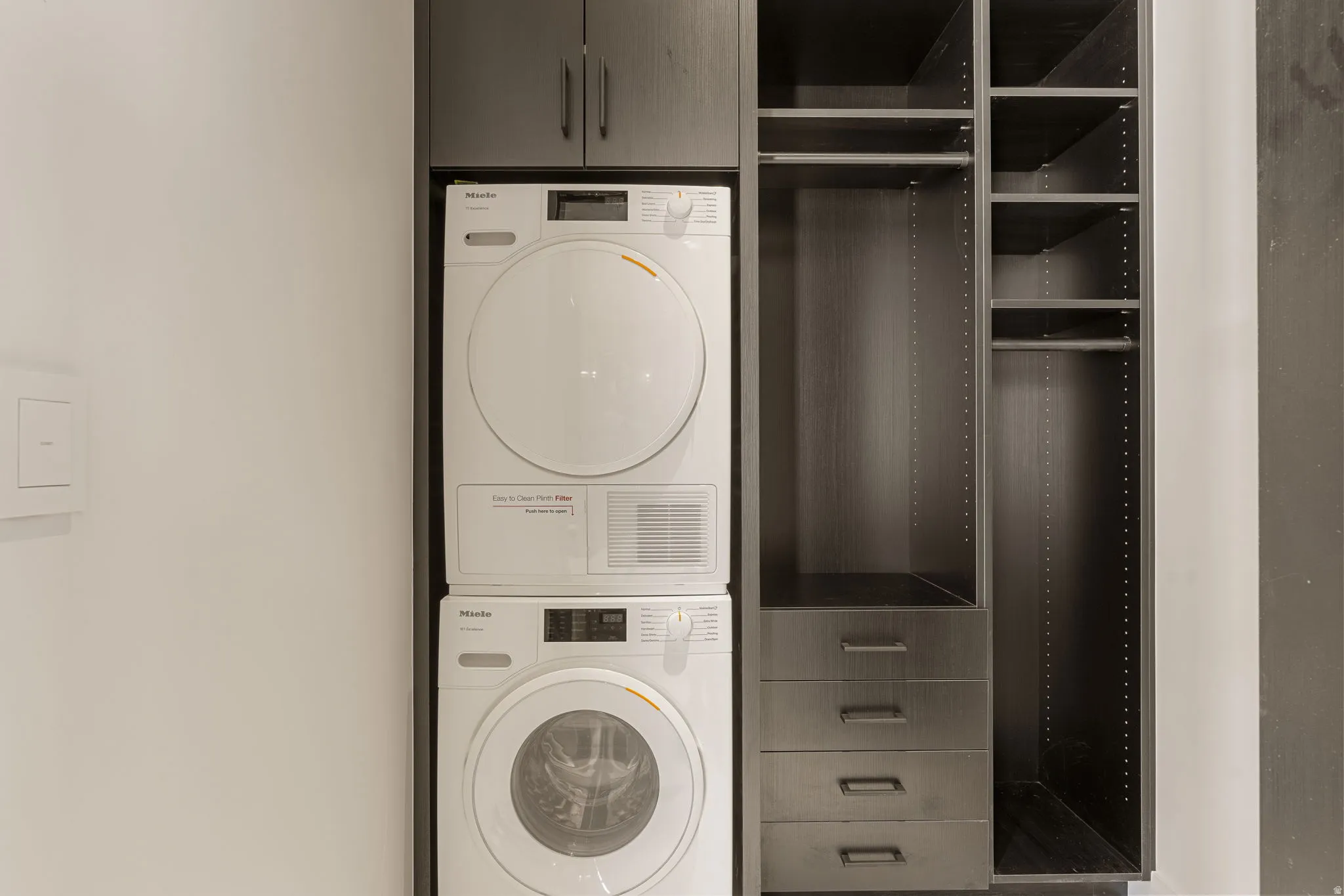 Stacked washer and dryer unit, built-in dark wood-finish cabinetry, and custom closet system with hanging rods and drawers
