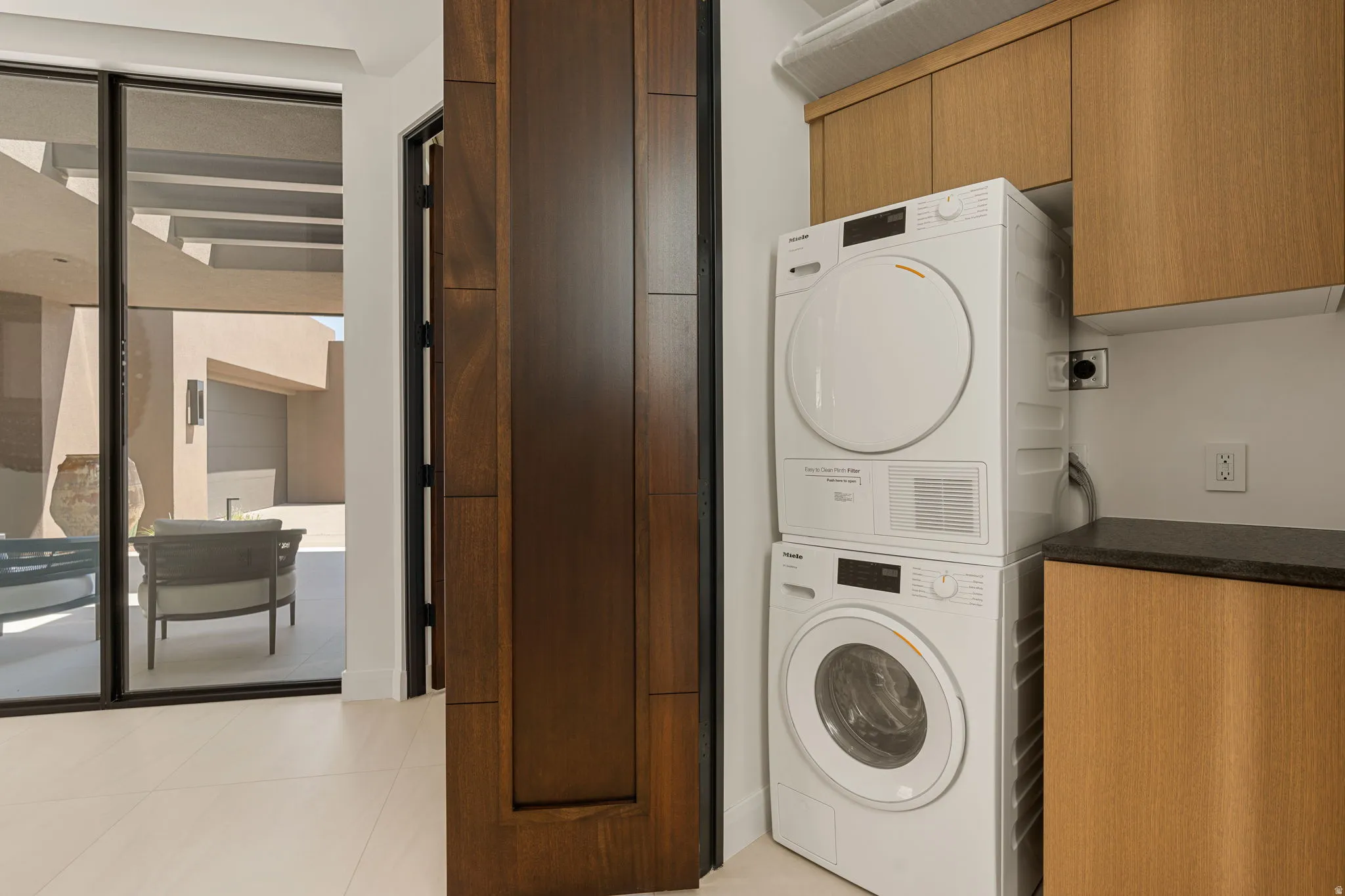 Laundry area with stacked appliances, wood-finish cabinetry, and dark stone countertop