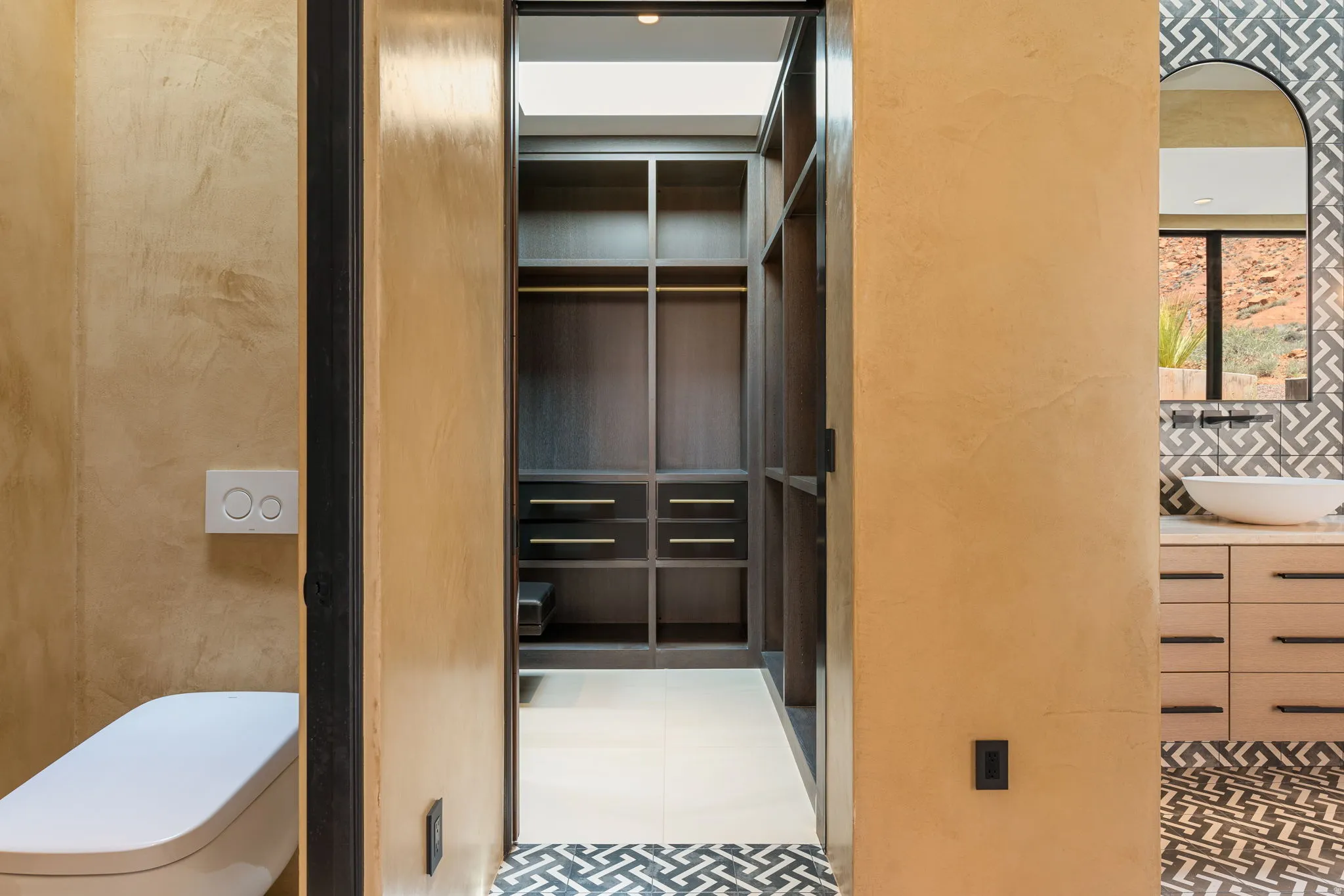 Built-in closet system, dual flush toilet, vanity with vessel sink, patterned floor tile, and wall-mounted faucet