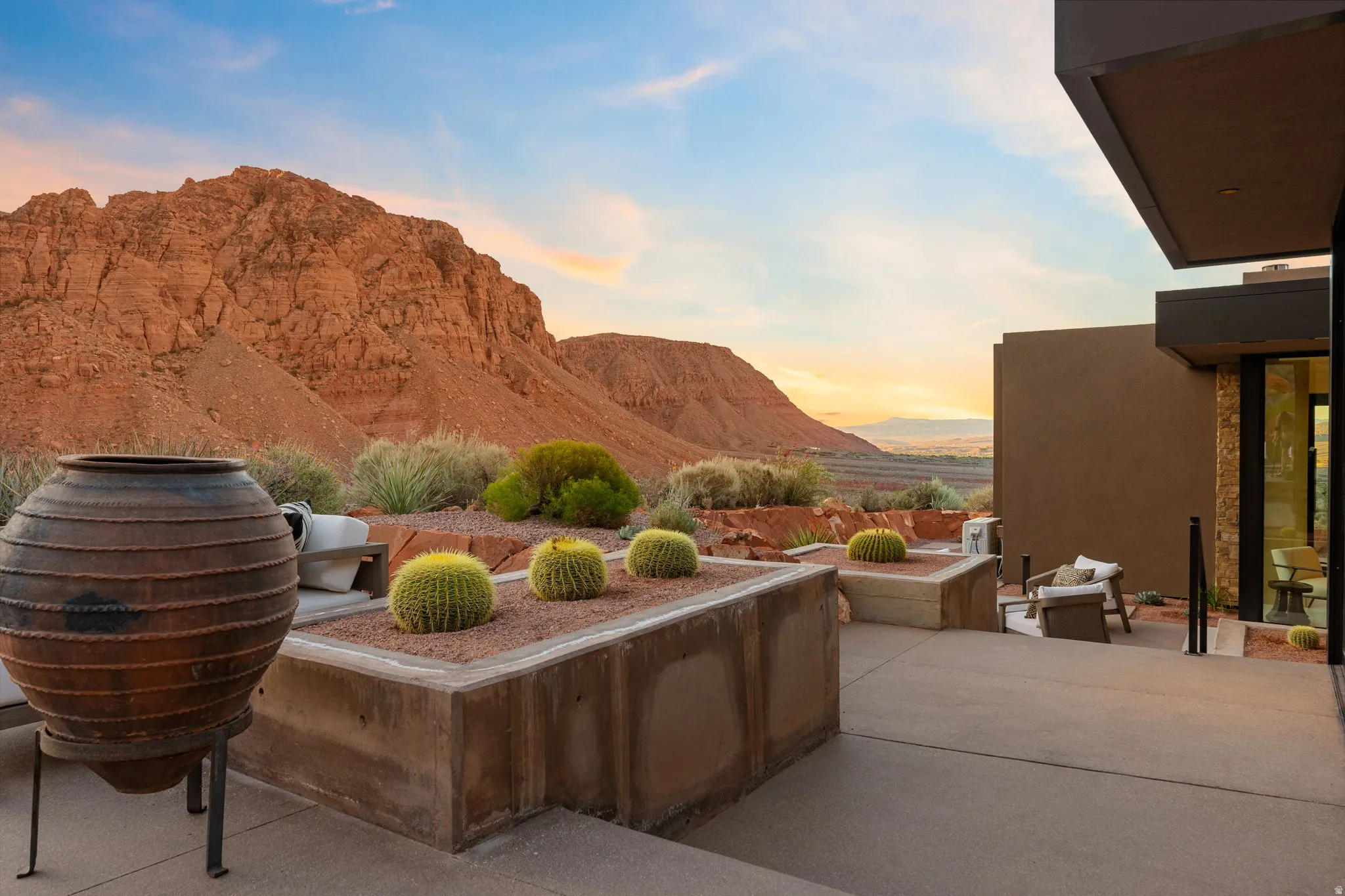 Expansive concrete patio with integrated planters featuring desert landscaping, natural rock formations, and distant mountain scenery